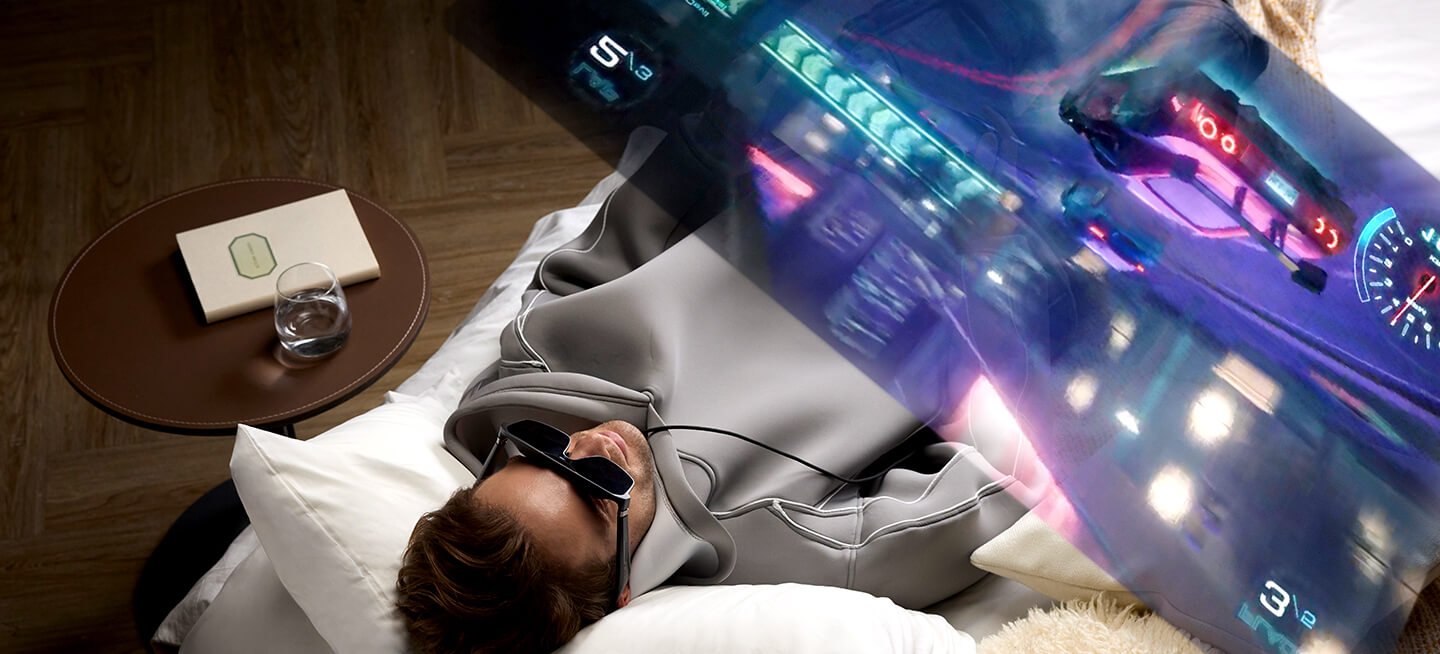 A man lying on the bed enjoy his immersive gaming experince with ROG XREAL R1 gaming AR glasses and ROG Xbox Ally.